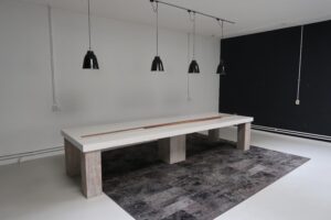 Lange witte tafel met houten poten onder vier zwarte hanglampen in een minimalistisch interieur aan het Gedempt Hamerkanaal.